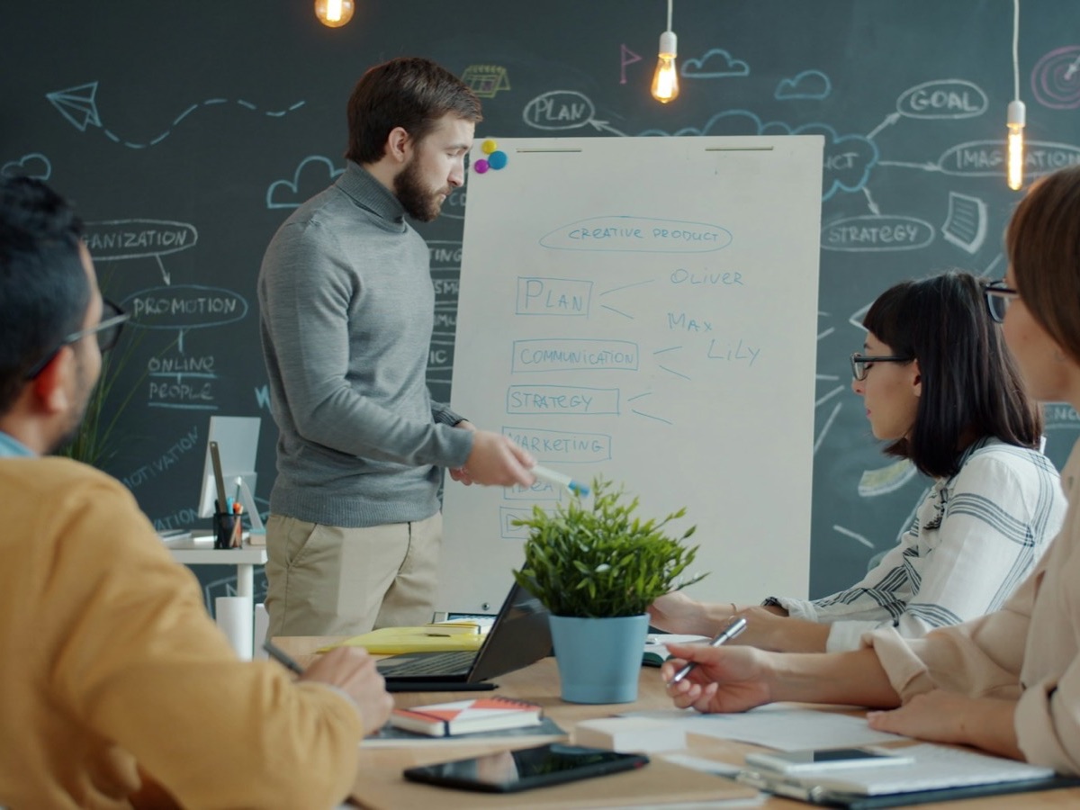 A man explaining a plan at a chalkboard wall to colleagues at a table
