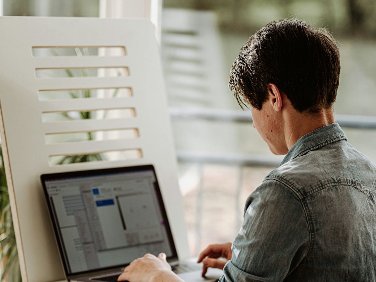 A person working at a laptop on a shelf by a window