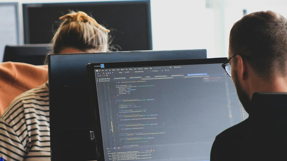 Two engineers at their monitors in a bright office, working through code together