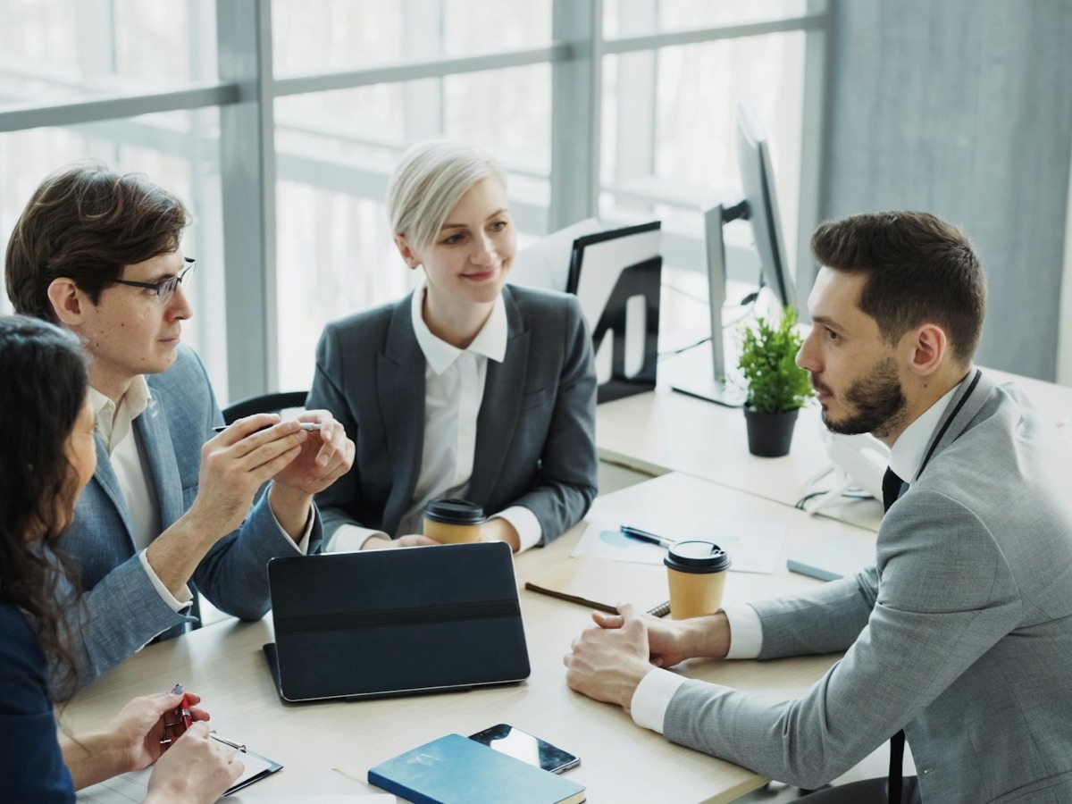 Four colleagues in a review meeting at a desk, one with a tablet