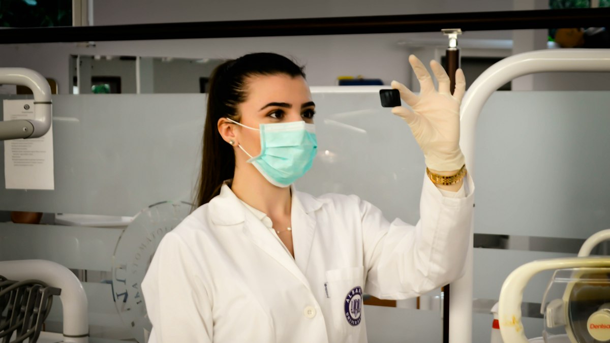 A scientist in a mask and gloves holding up a sample in a laboratory